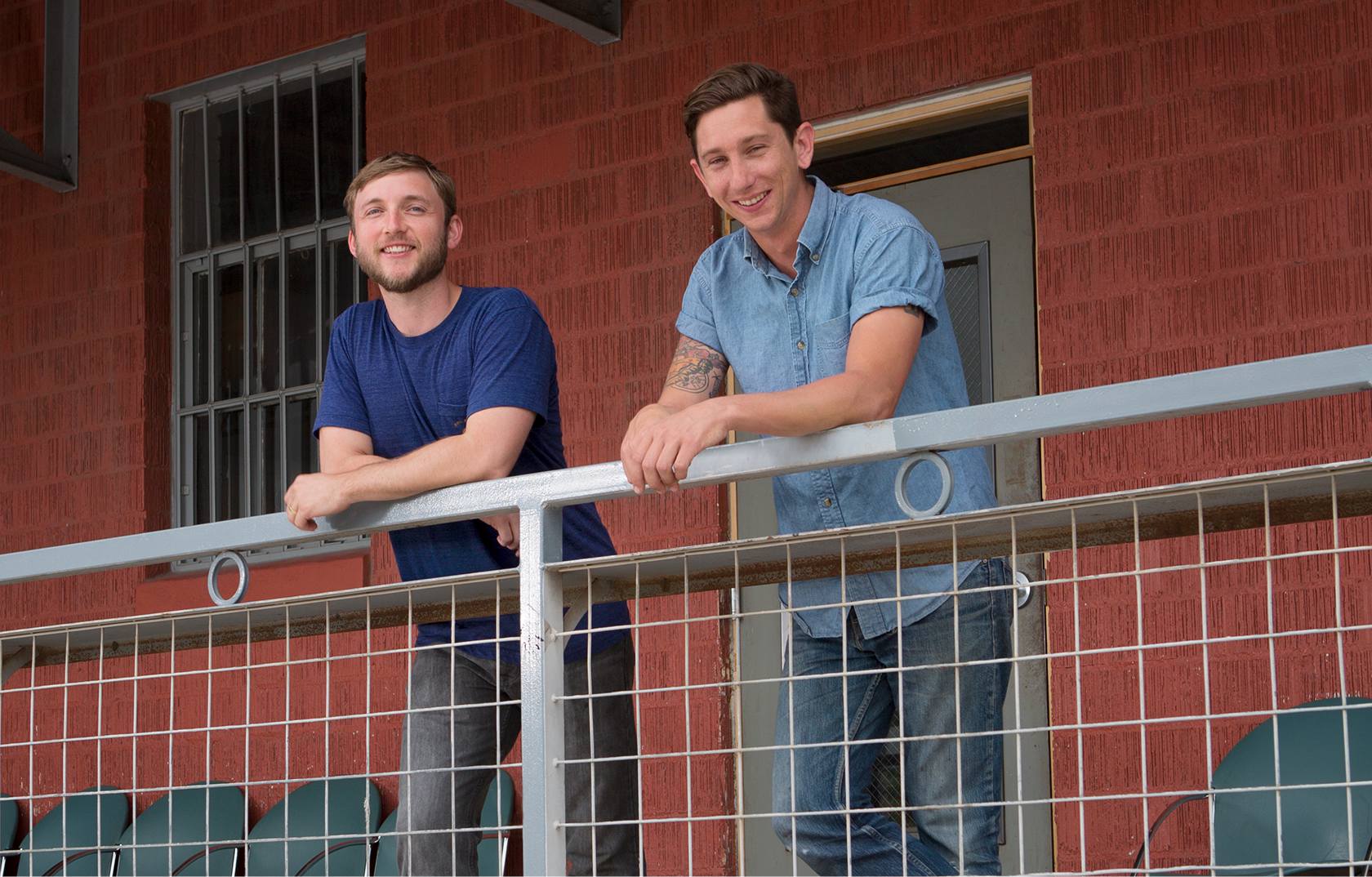 Two men smiling and leaning on a railing
