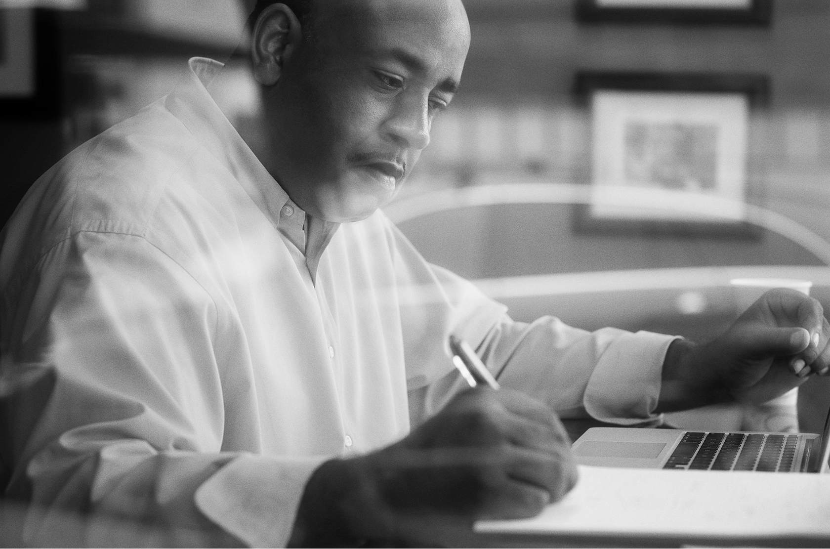 Man using a laptop and writing on a notepad